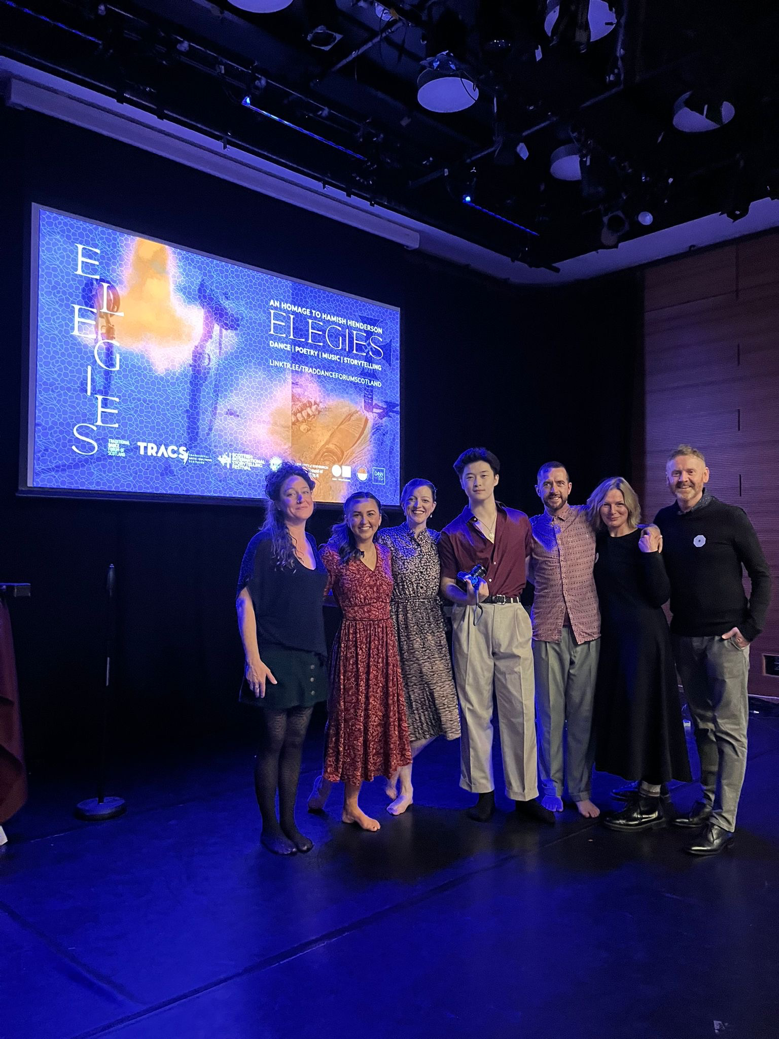 The Elegies company after a performance, with the production projection behind them