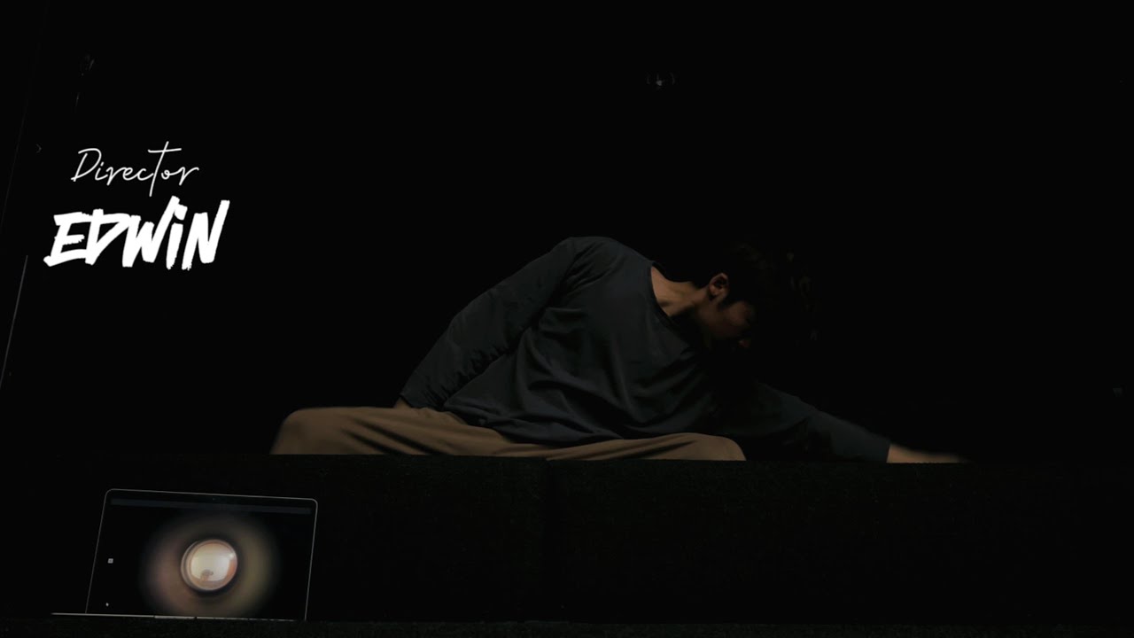 A dancer folded forward beside a glowing laptop on a dark stage